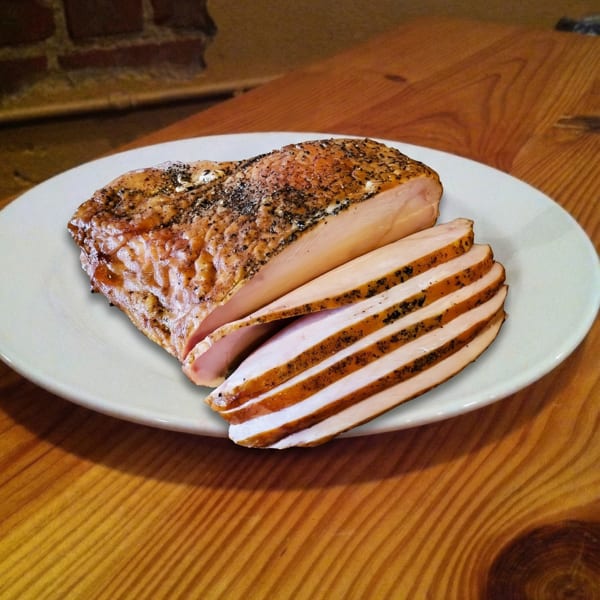 Seasoned, sliced smoked chicken breast on a white plate, resting on a rustic wooden table.