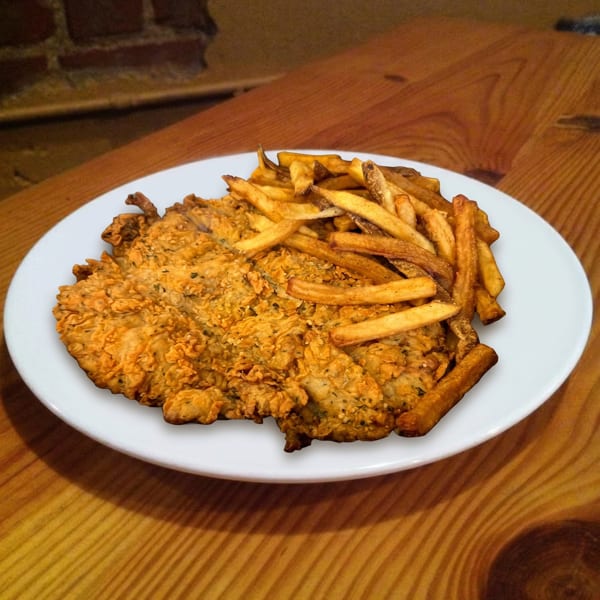 Crispy fried chicken cutlet and golden french fries on a white plate, on a wooden table.