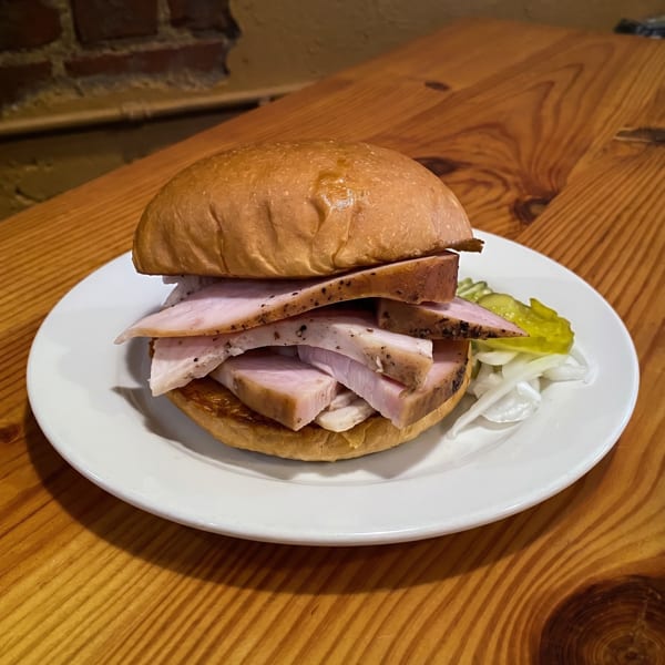 A turkey sandwich with pickles and onions on a white plate, on a wooden table.