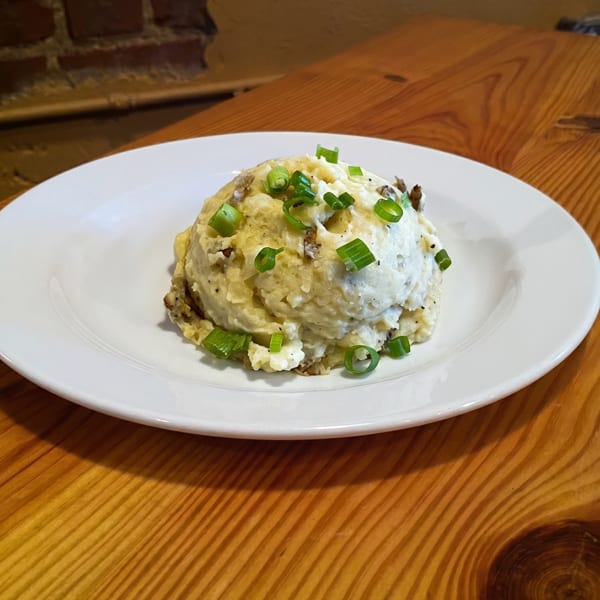 A serving of mashed potatoes topped with chopped green onions on a white plate.
