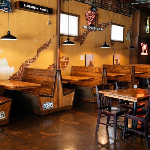 Restaurant interior with wooden booths and tables, exposed brick, and neon signs on a distressed yellow wall.